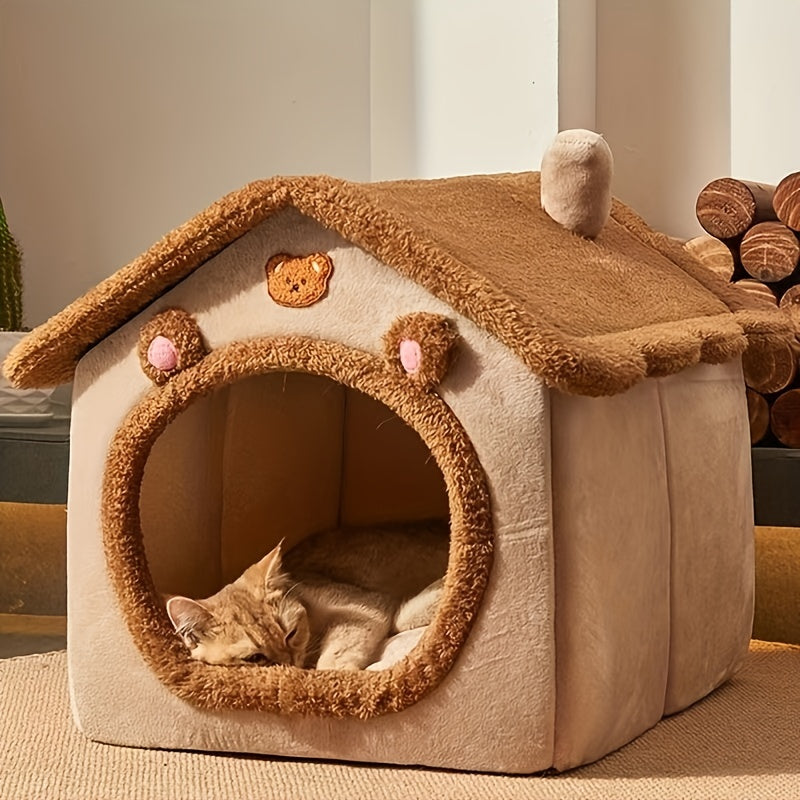 Cat lying inside a plush, doghouse-shaped pet bed with teddy bear ears and a chimney.