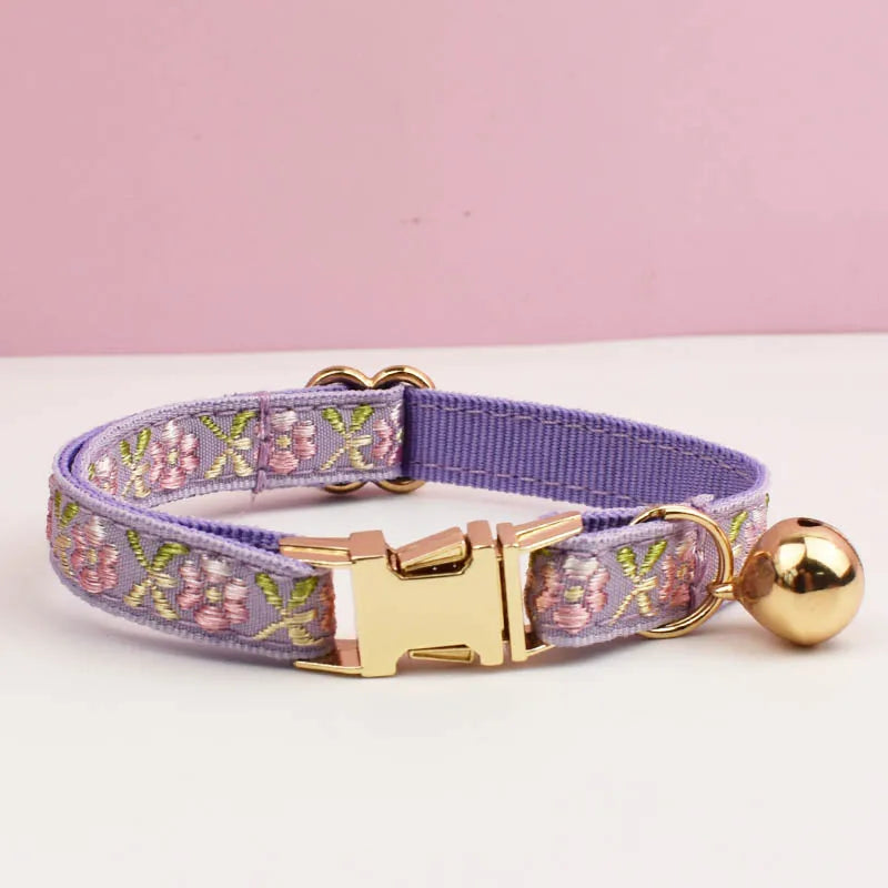 Lavender dog collar with floral pattern and gold hardware on a white surface with pink background