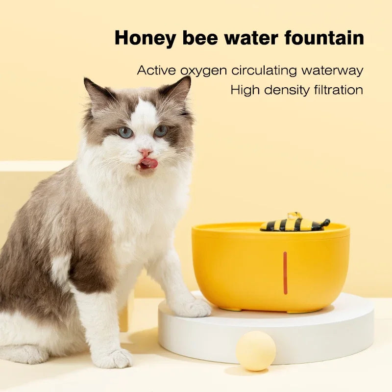 Cat next to a yellow water fountain with honey bee design on a beige background